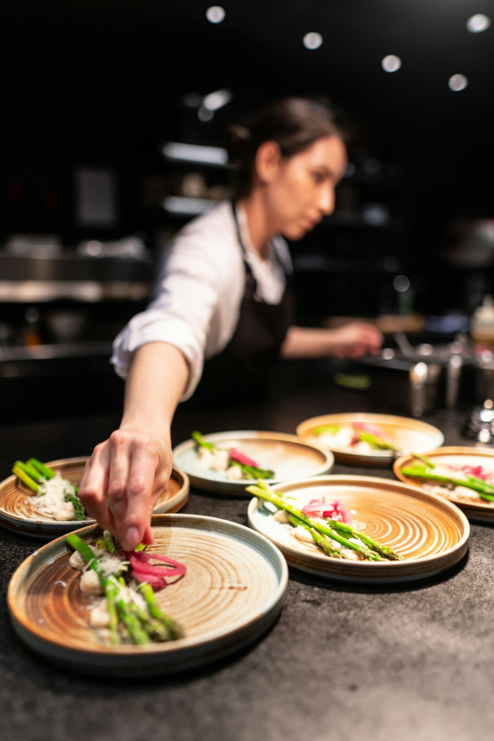A chef finishing a row of plates in a busy kitchen