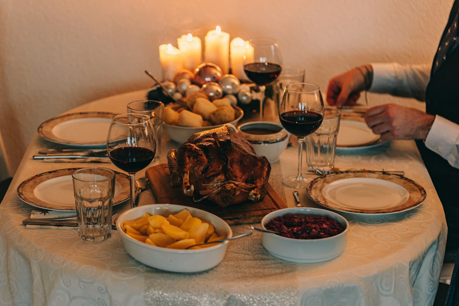 A candlelit round table set for four with a roast turkey, potatoes and cranberry sauce